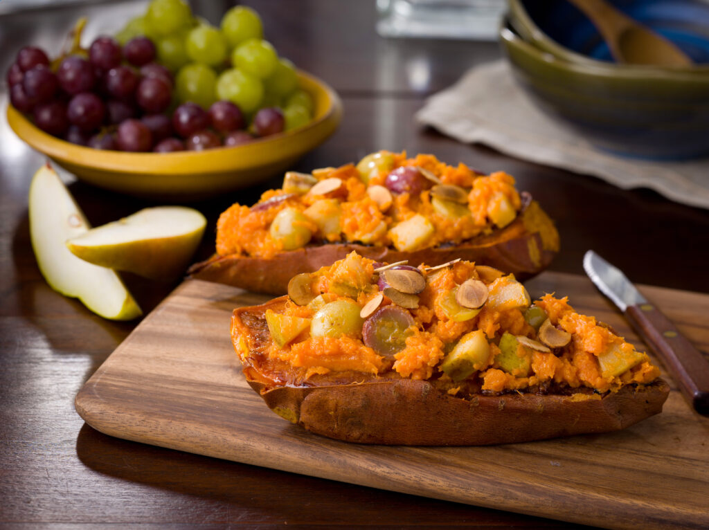 stuffed sweetpotatoes with roasted grapes, nuts on a board with a knife; bowl of red and green grapes behind