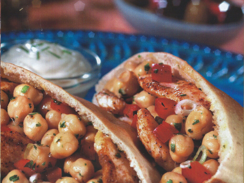 Two pitas with chicken and garbanzos on a blue plate with yogurt sauce