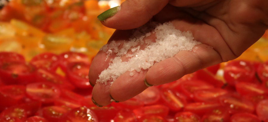 Hand adding salt to halved red and yellow cherry tomatoes
