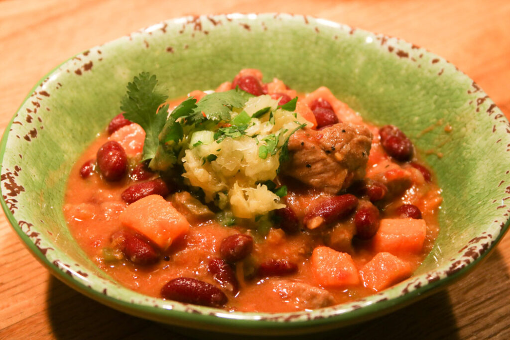 Green bowl filled with CaribBean One Pot Wonder, with pork, sweet potatoes, kidney beans and topped with pineapple salsa