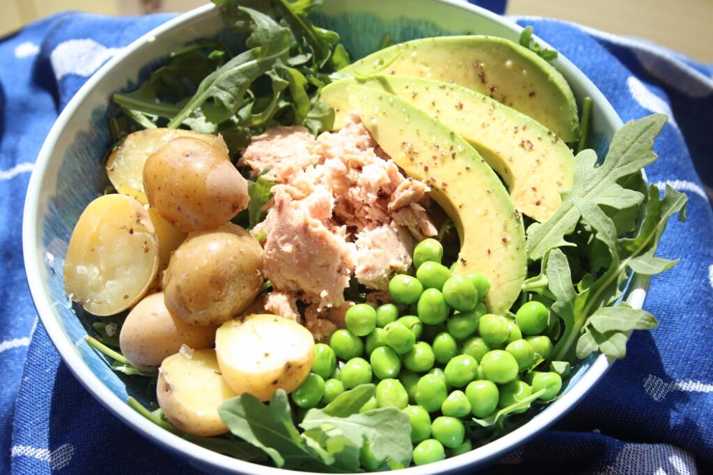 overhead shot of blue and white bowl filled with peas, arugula, avocado slices, tuna and new potatoes
