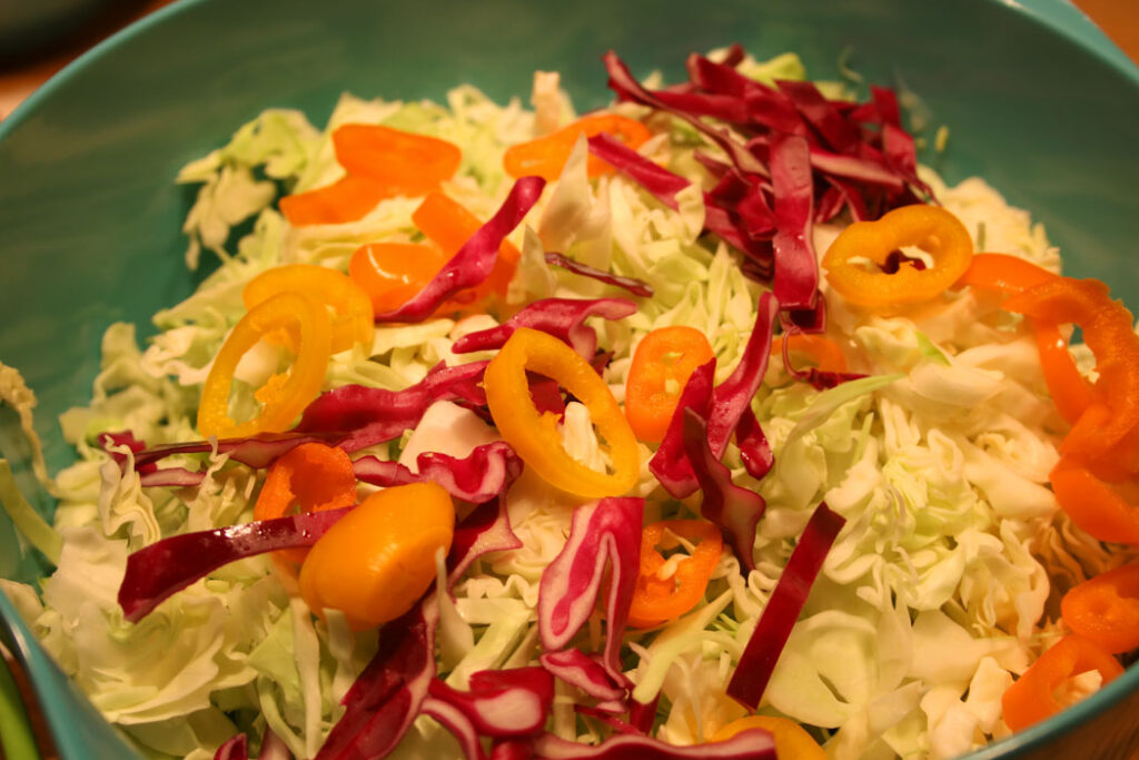 Firecracker Cole Slaw in the Making: shredded green and red cabbage, rings of mini sweet peppers