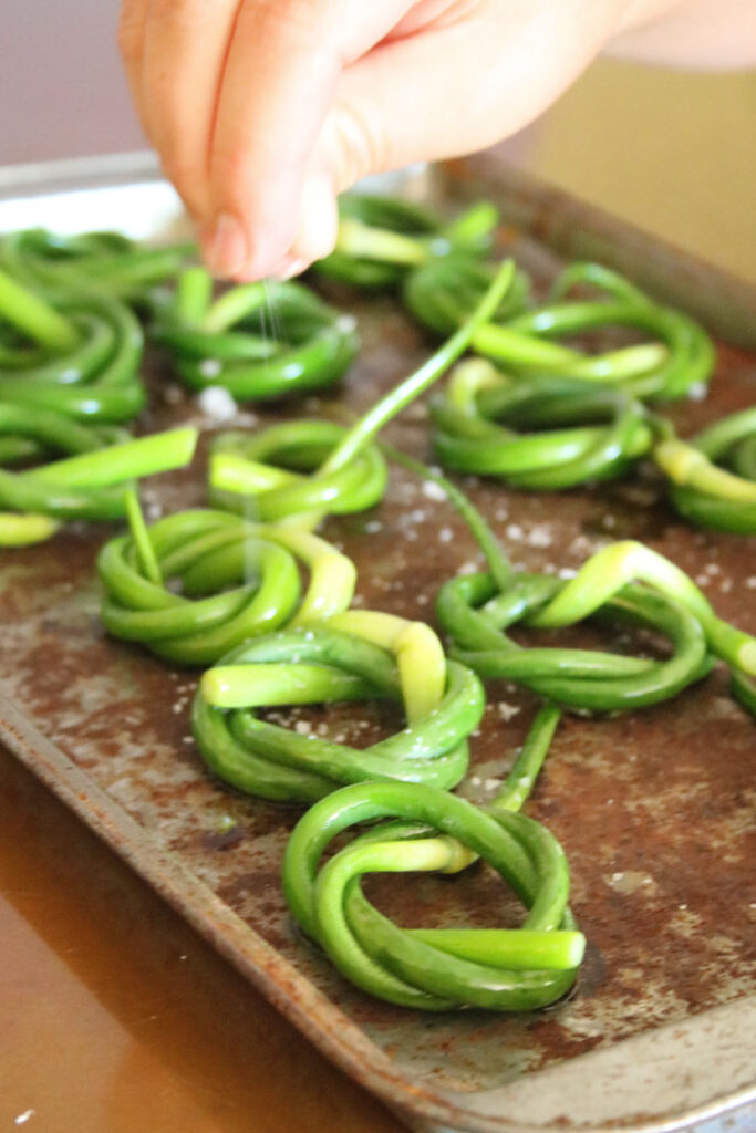 Garlic Scape Bundles on a sheet pan being sprinkled with salt