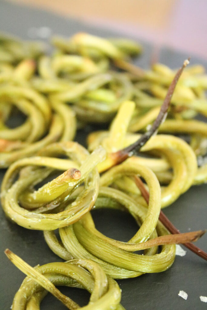 Bundles of roasted Garlic Scapes with sea salt on black slate tray