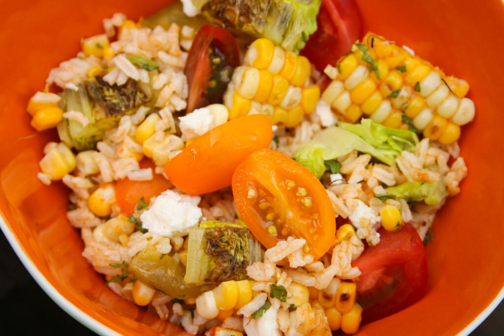 rice, grilled veggie, salad with chunks of grilled corn, and cherry tomatoes in an orange bowl