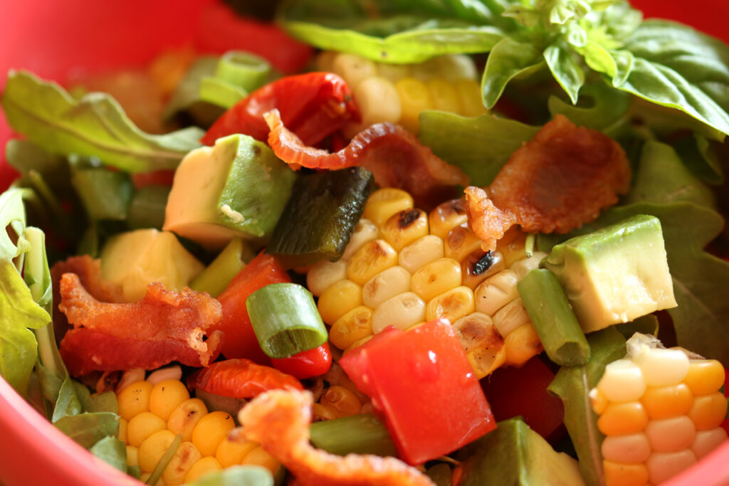 Everything But The Farmer Farmer\'s Market Salad in a red bowl: grilled corn, avocado, bacon, scallions, tomatoes and basil
