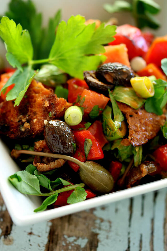 Rustic Bread Salad in a square white bowl with olives, caper berries, bread, scallions and tomatoes