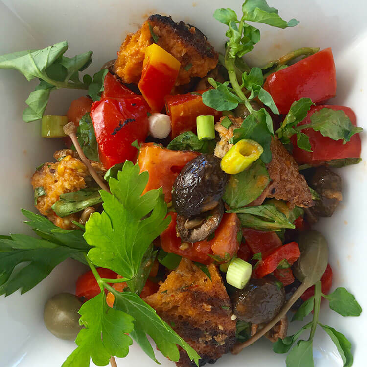 Rustic Bread Salad in a square white bowl with olives, caper berries, bread, scallions and tomatoes