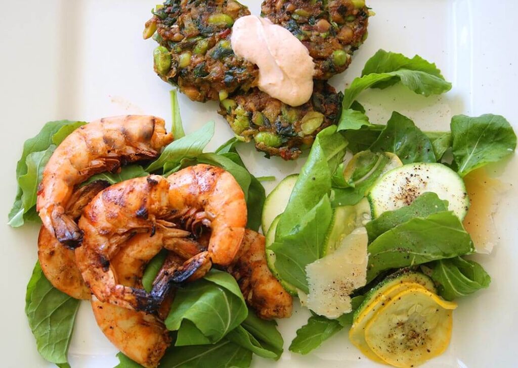 overhead shot of a white plate filled with Summer Squash Salad, edamame fritters and spicy grilled shrimp