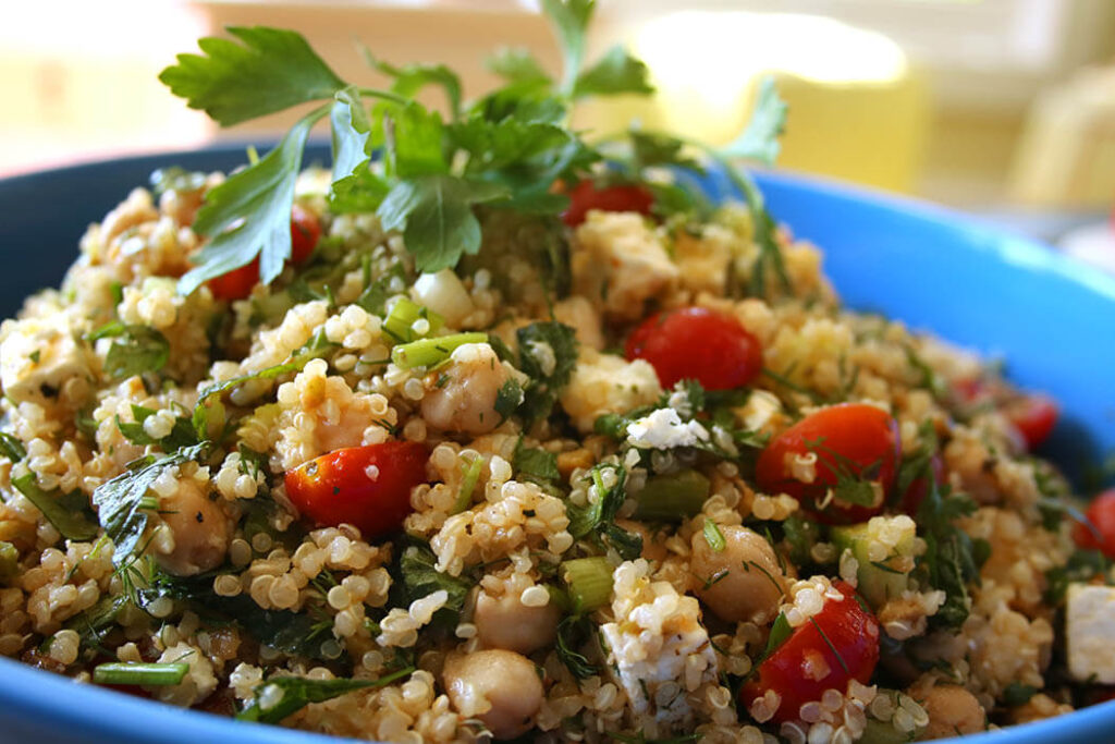 Quinoa Greek Salad in a blue bowl with feta, tomatoes, cucumber, scallions and parsley