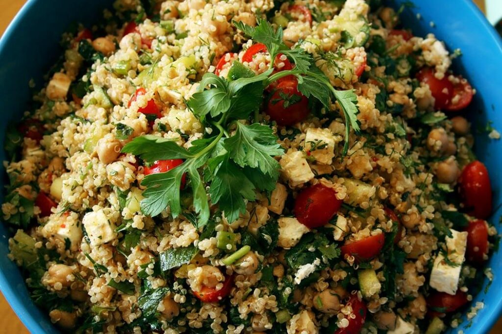 Quinoa Greek Salad in a blue bowl with feta, tomatoes, cucumber, scallions and parsley
