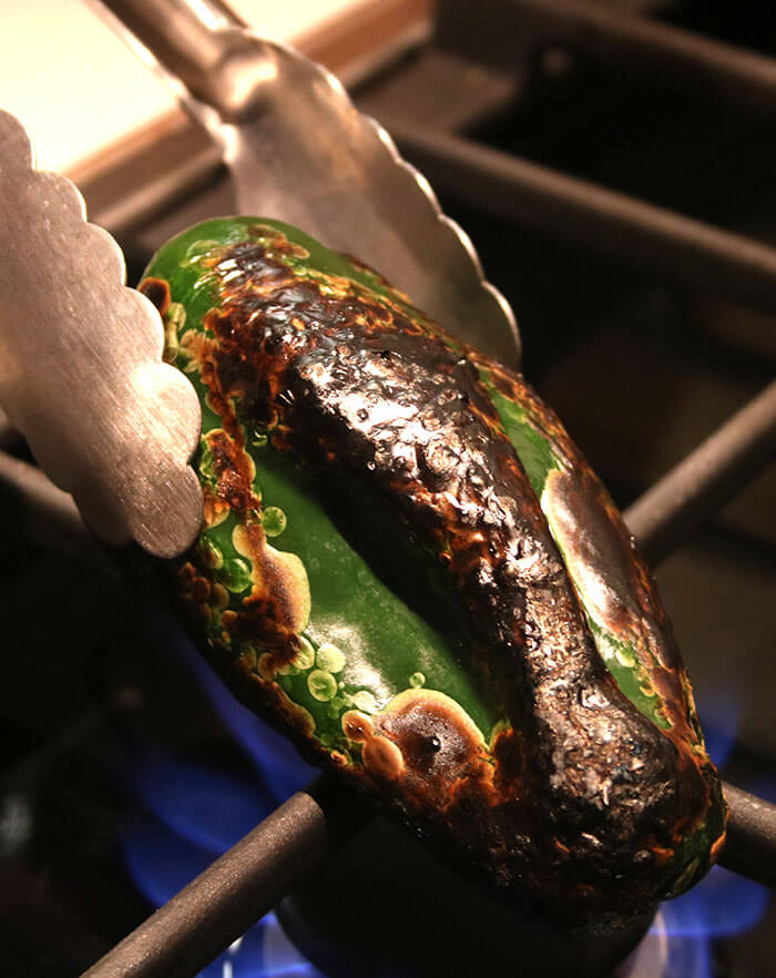 Roasting Poblanos on an open flame with tongs
