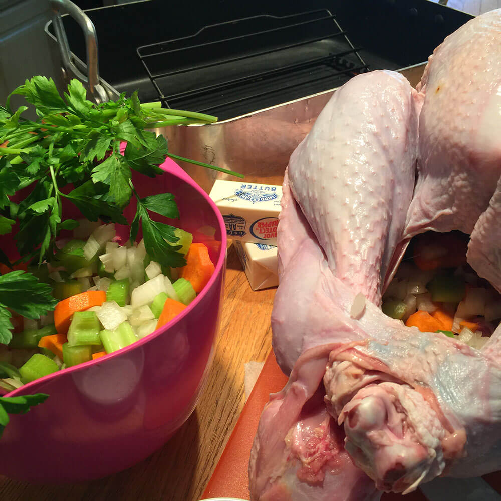 Prepping the turkey, roasting pan, butter, and a pink bowl of carrots, onions, celery and parsley
