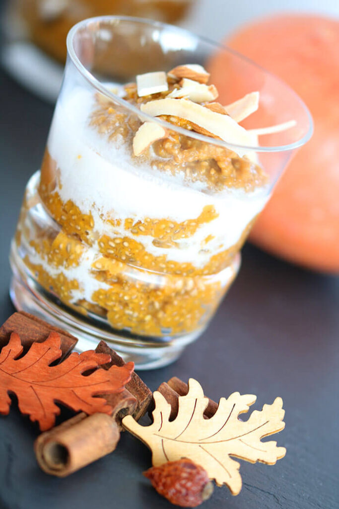 Fall Chia Pudding in a glass with coconut milk, with fall leaves, cinnamon bark and a pumpkin