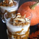Pumpkin Chia Pudding in glasses topped with coconut milk, coconut strips, and almonds with a pumpkin behind