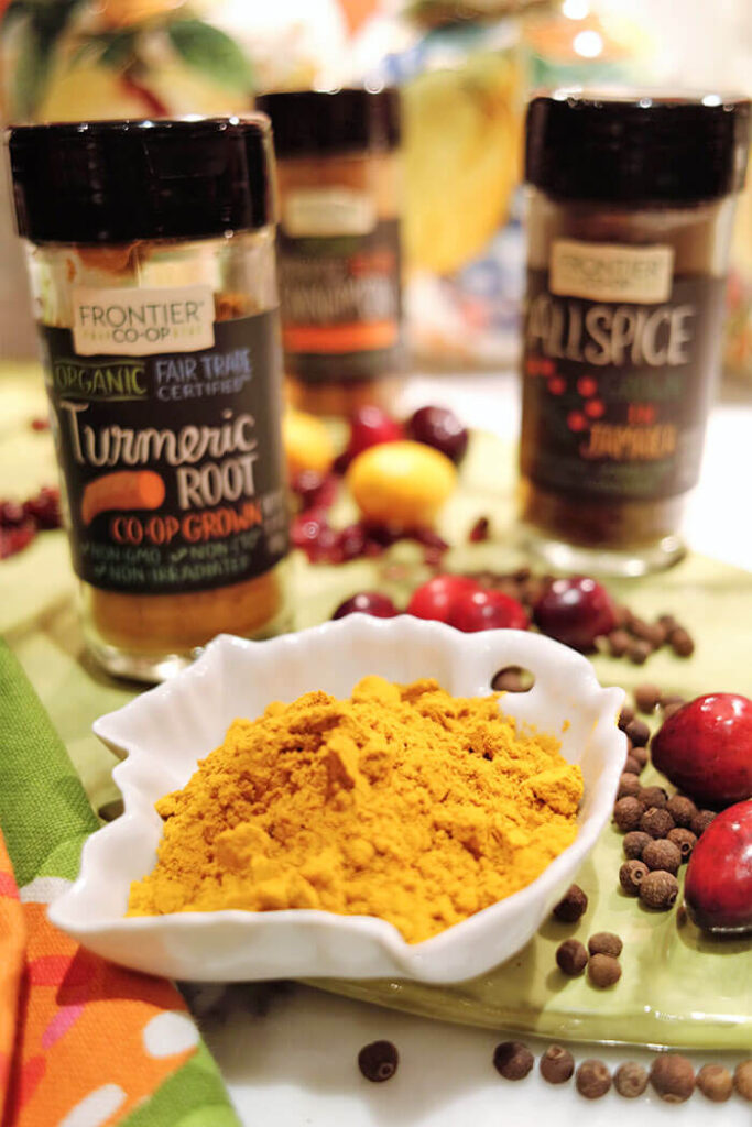 Frontier Coop Spices with a white bowl of ground turmeric and allspice berries with fresh cranberries and kumquats