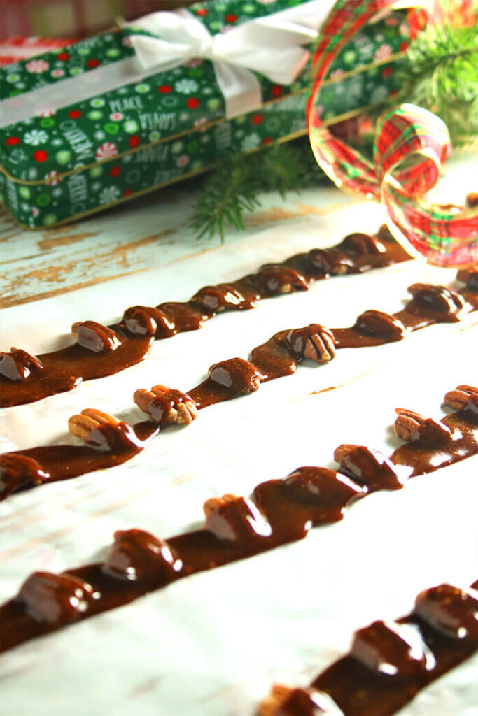 Toffee drizzle over rows of pecans with christmas tins behind