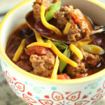 Cutty Sark Kick Off Chili in a Mug with yellow rim and red and blue pattern, and a spoon close up of chili with scallions and cheddar