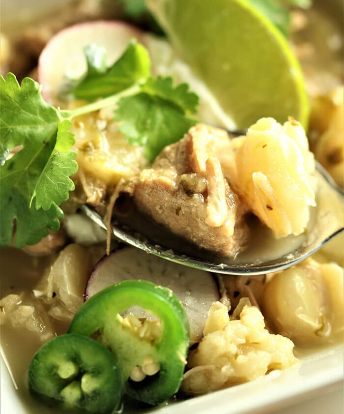 spoonful of pork and polose with lime and cilantro garnish and sliced jalapeno