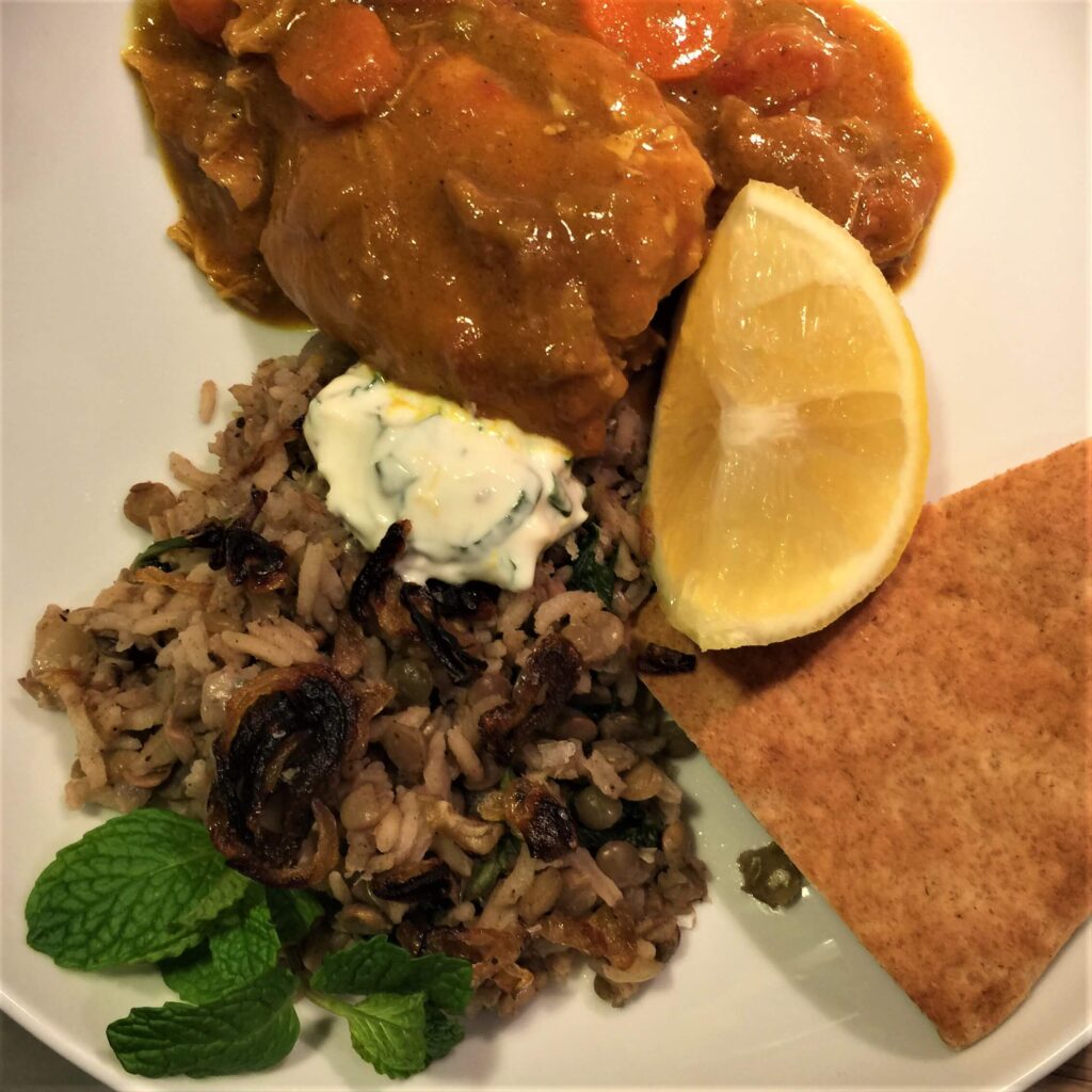 Curried Chicken Thighs and Mujadara on a plate with lemon, yogurt sauce and pita