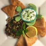 Overhead shot of mujadara with pita, a turtle shaped bowl with yogurt dip, lemon and fresh mint