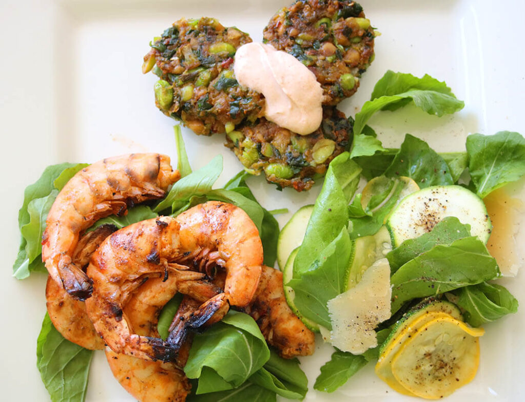 over head shot of white plate with salt and pepper shrimp, edamame fritters with chipotle aioli and zucchini and arugula salad