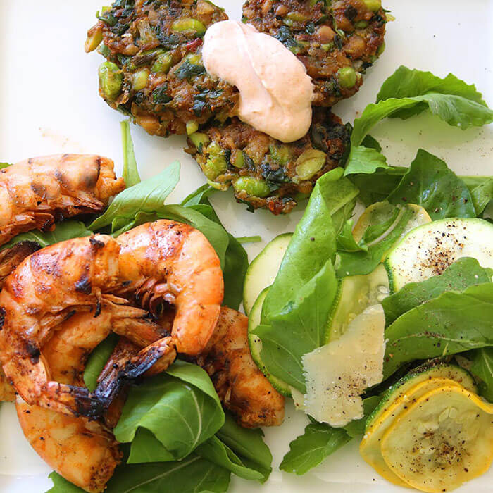 over head shot of white plate with salt and pepper shrimp, edamame fritters with chipotle aioli and zucchini and arugula salad