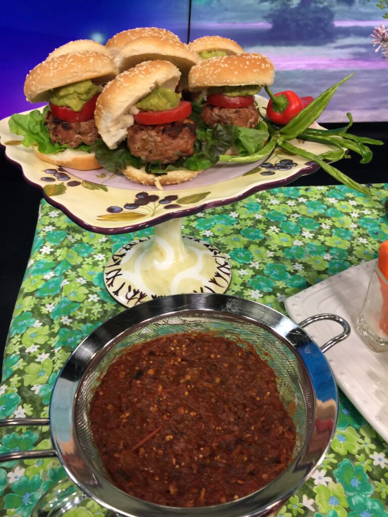 Draining Salsa to Make Turkey Burger - in a sieve with a platter of turkey burger sliders behind