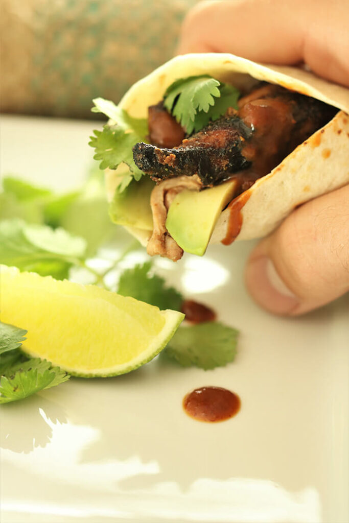 Hand holding a fig marinated chicken fajita with avocado, garnished with lime and cilantro