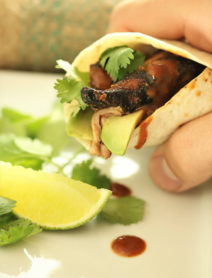 Hand holding a fig marinated chicken fajita with avocado, garnished with lime and cilantro