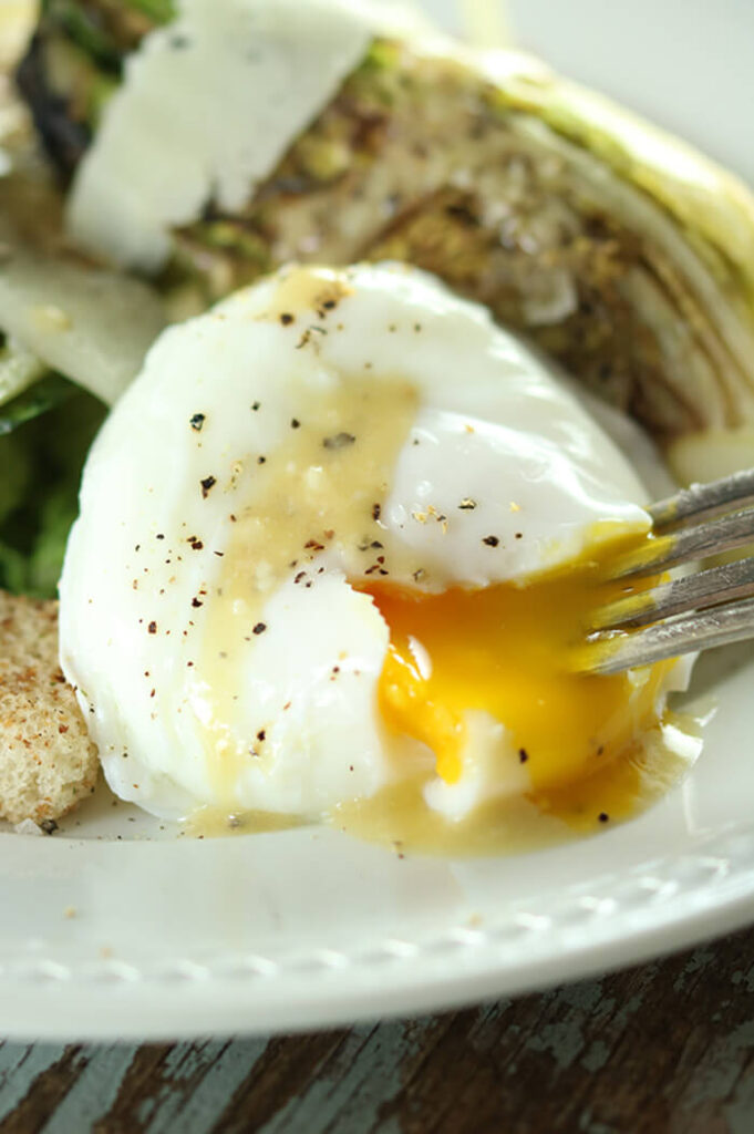 Poached Egg close up on Caesar salad; white plate and a fork