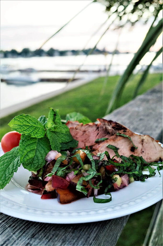 Asian Marinated Pork Tenderloin and Ginger Plum Salsa on a white plate with a lake in the background