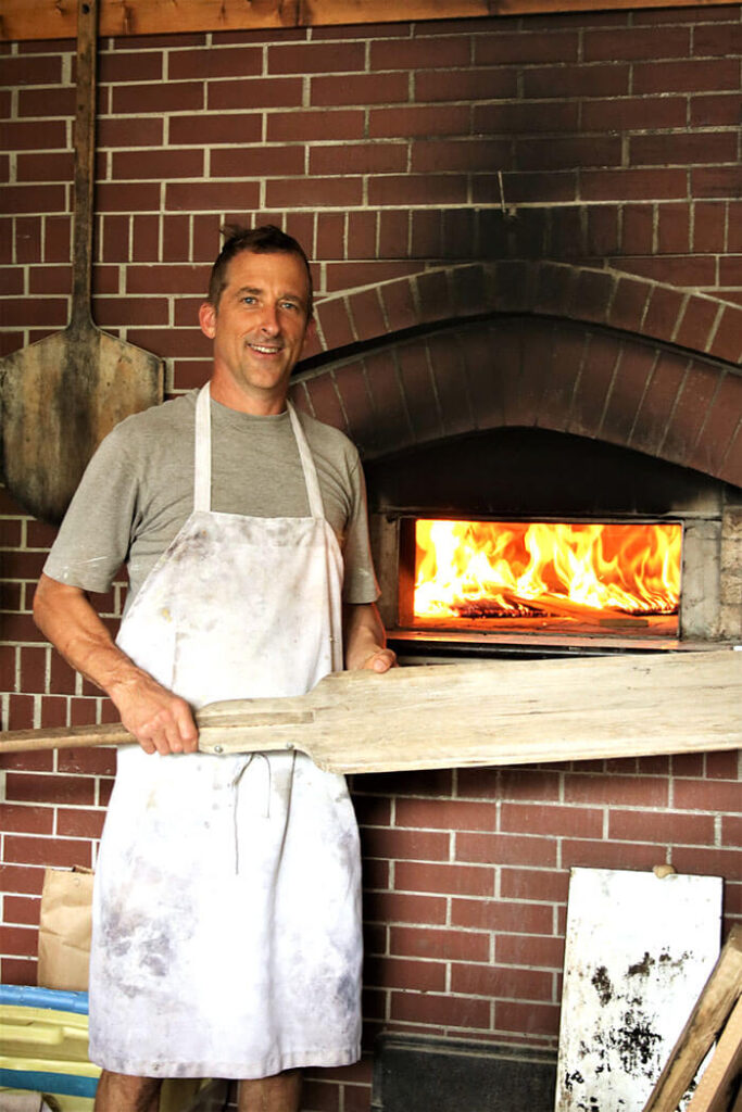 Charlie Muller with a peel in front of the wood fired oven