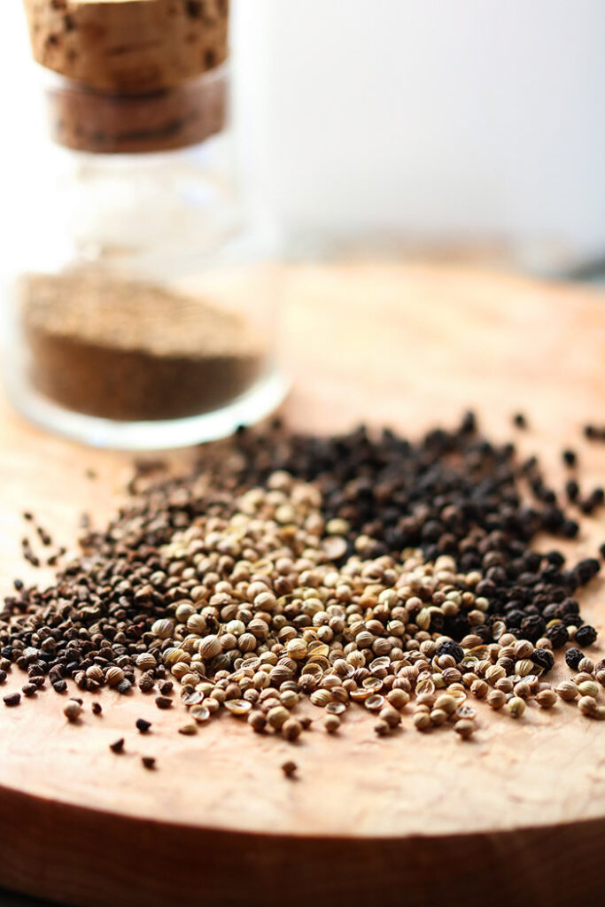 Pepper, Coriander, Cardamom on a wooden board with a jar in the background