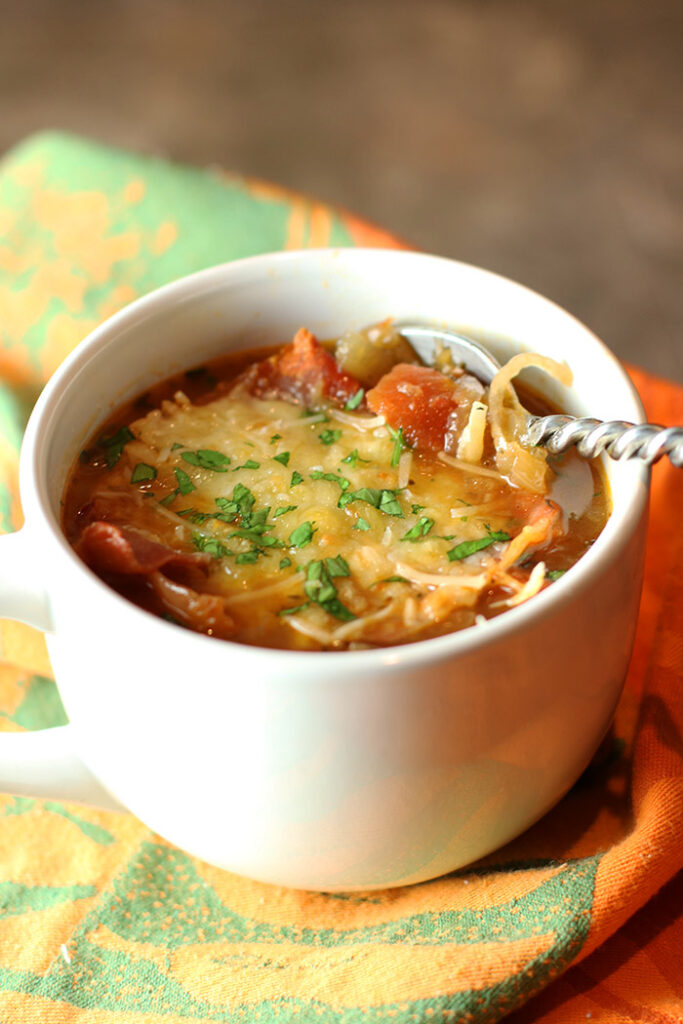 3 Onion Soup in a white mug with a spoon. Close up of the Prosicutto Gruyere Topping