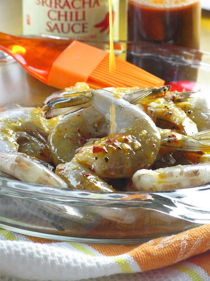 Glass plate with shrimp marinating, orange basting brush, sriracha  and tobasco