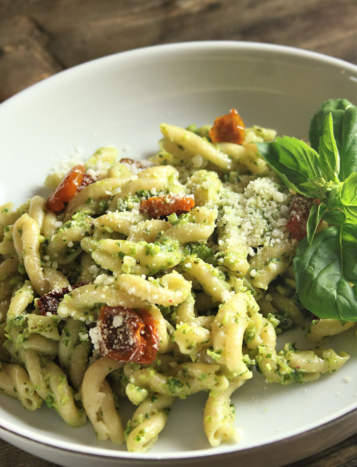 Scape Pesto on gemelli pasta with oven dried tomatoes in white bowl, garnished wit basil sprig