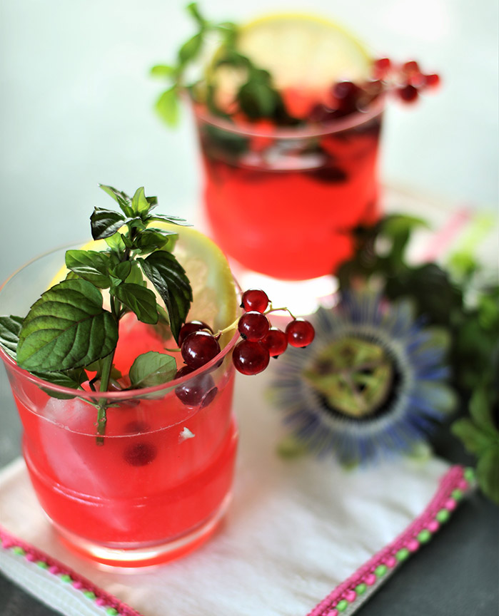 two glasses of red currant lemonade with mint, currant, lemon slice garnish