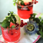 two glasses of red currant lemonade with mint, passion vine flower on white napkin with pink trim