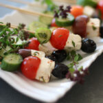 Greek Salad Salad on a Stick: marinated cucumbers, cherry tomatoes, feta and black olives on a white tray with fresh thyme