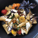 Close up of Skillet Burst Tomatoes Pasta with Fresh Mozzarella in a black bowl with opal basil