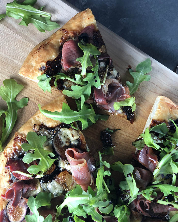 Fig, Cambozola and Prosciutto Pizza with Arugula with a slice out - overhead shot and close up