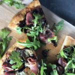 Fig, Cambozola and Prosciutto Pizza with Arugula with a slice out - overhead shot and close up