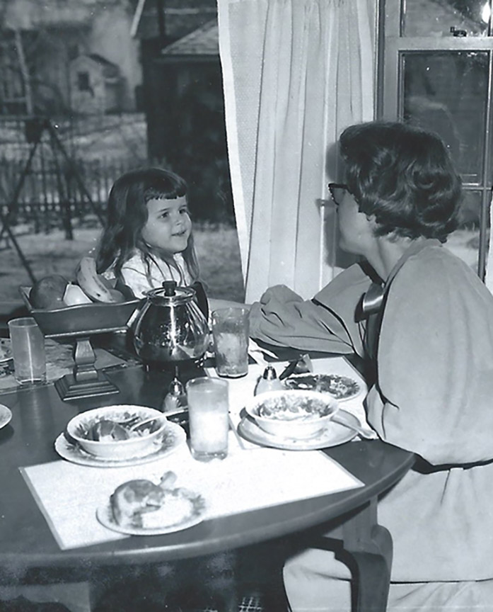 Katy and her mom sitting at the breakfast table in the 50th. Table set with cereal bowls, glasses of milk and coffee pot
