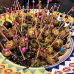 Fit for Diwali:  Indian Spiced Potatoes in a multi color bowl with a tile pattern, with lots of toothpicks with colorful bells