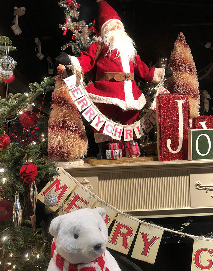Foodie's Best Gift Guide: Christmas window display of a santa holding a merry christmas banner on a desk, with a white bear in a red striped scarf