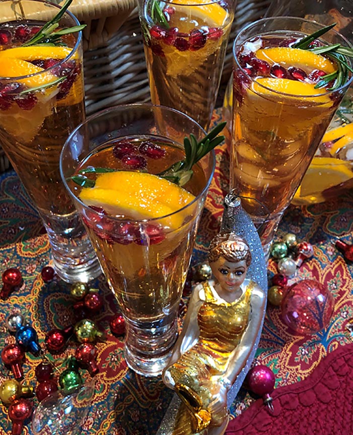 Santa Sparkler cocktail in tall glasses on a brocade cloth with Angela Lansbury ornament and multi color small balls