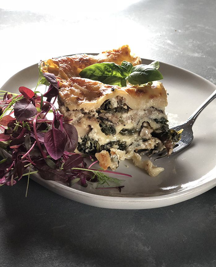 Shiitake Kale Lasagna on a white plate with a fork and micro green salad