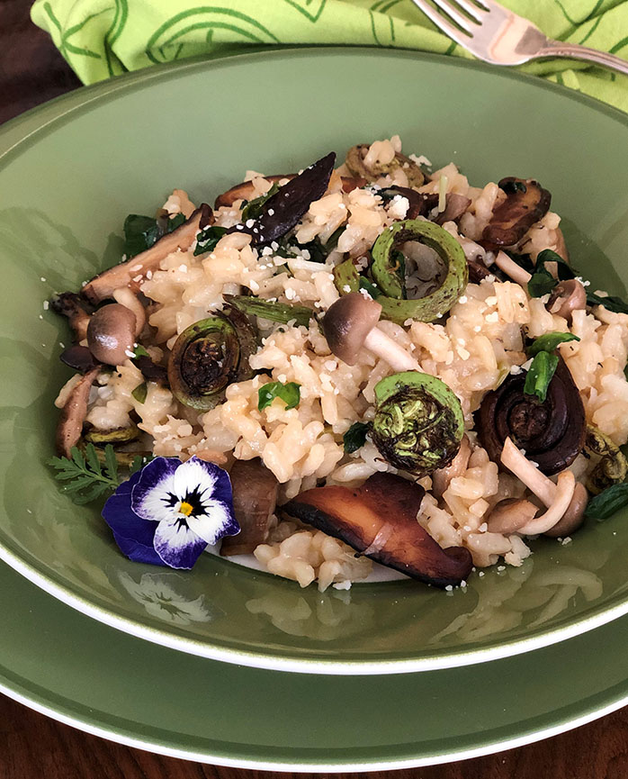 Mushroom risotto in a green bowl with pansy garnish and parmesan sprinkle with green napkin and fork