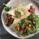 Salsa Verde Fajita: white plate with a flour tortilla, grilled vegetables and chicken, sauced with salsa verde and accompanied by an arugula, corn, tomato and avocado salad